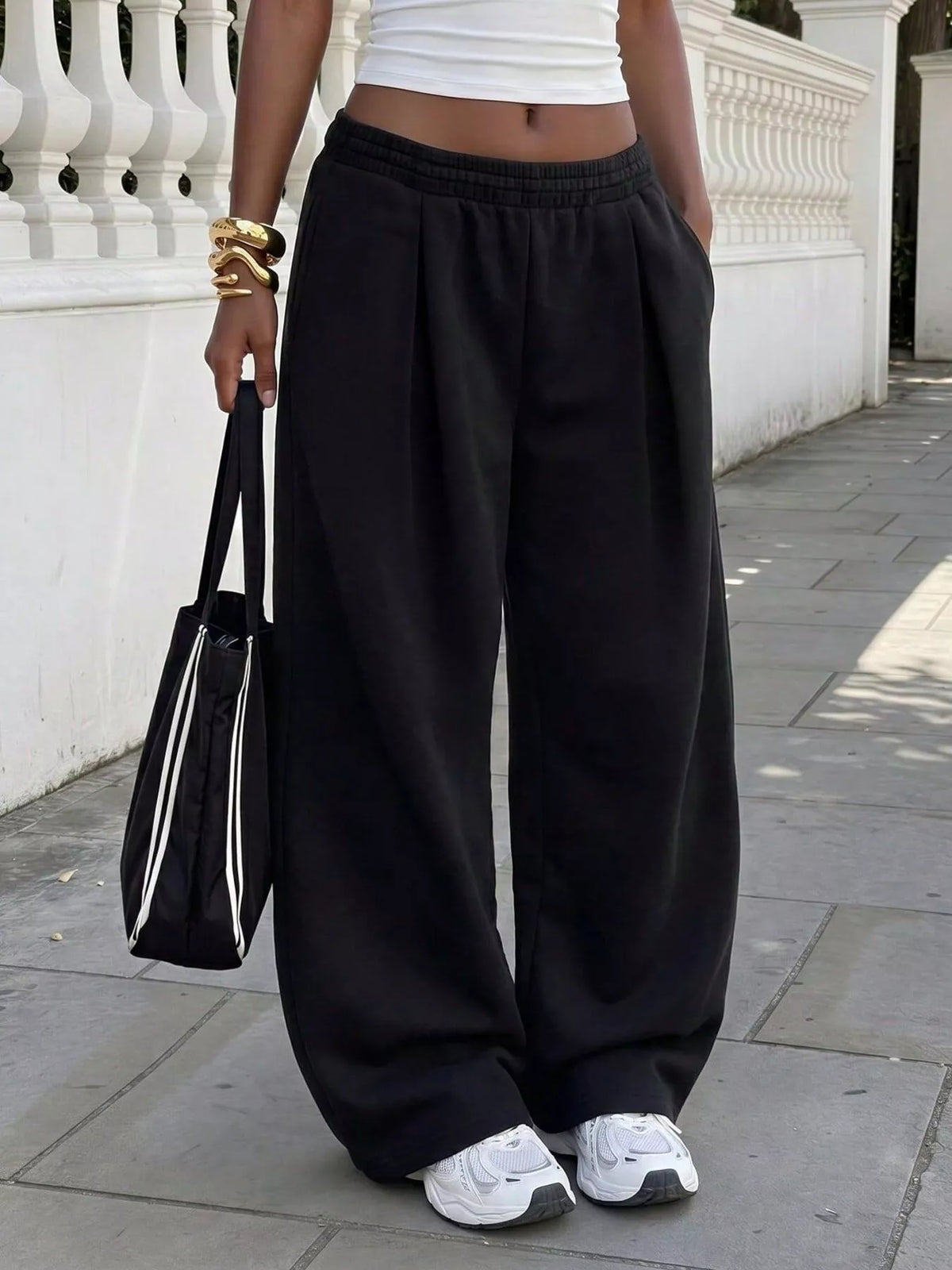Front view of black wide-leg sweatpants with front pleats, styled with a white cropped top and sneakers.